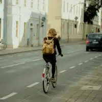 Femme circulant à vélo en ville sur une chaussée partagée avec les voitures, illustrant les conditions réelles de déplacement des cyclistes urbaines.