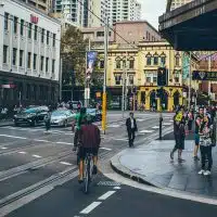 Cycliste circulant en centre-ville de Sydney au milieu des piétons et du trafic, illustrant la cohabitation des mobilités urbaines.