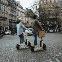 Deux usagers circulant en trottinette électrique sur une place urbaine française, illustrant la cohabitation avec les autres usagers et le débat autour de la réglementation et de l’immatriculation.