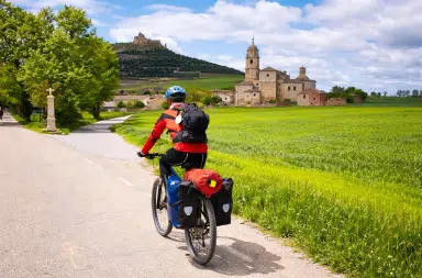 Cycliste en voyage à vélo traversant un paysage français avec village historique en arrière-plan
