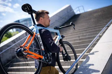 Homme portant un vélo électrique léger Electrolyte S4 E dans un escalier urbain