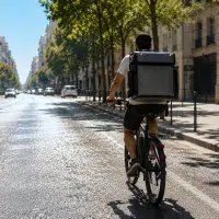Livreur à vélo roulant dans une rue de ville sous un soleil de canicule