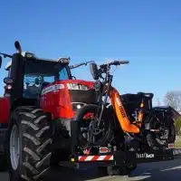 Vélo tout terrain électrique orange Agricycles fixé sur un support Tract'moi à l'avant d'un tracteur, sur une route de campagne